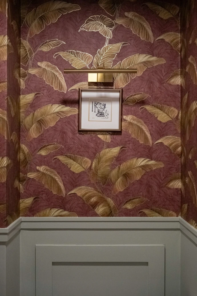 Framed artwork hangs on a wall with tropical leaf wallpaper.